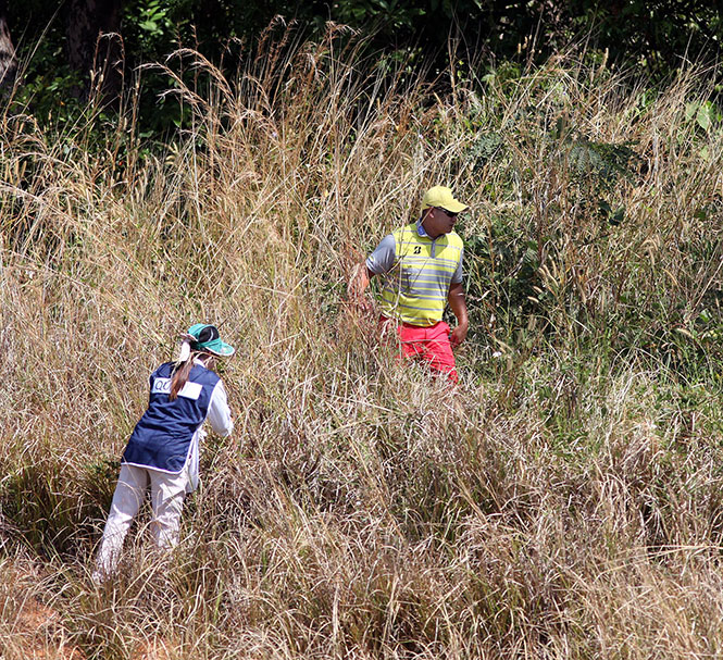 Angelo Que and his caddie search for the ball in tall grasses after an errant drive on No. 17